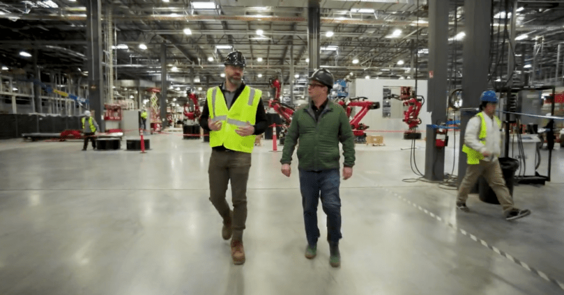 Ashlee Vance tours Tesla’s new dedicated Semi factory in Sparks, Nevada, alongside Dan Priestley, Tesla’s Semi program lead, as they walk the vast production floor surrounded by advanced red robotic arms preparing for full-scale all-electric truck assembly. Captured directly from Ashlee Vance’s Core Memory factory tour video — offering a rare inside look at the massive ramp-up of Tesla Semi production.