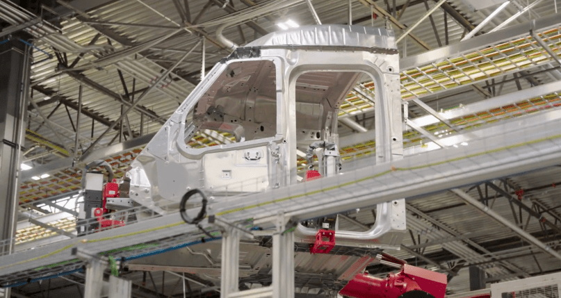 A bare silver Tesla Semi cab shell glides along the overhead conveyor in Tesla’s Sparks factory — raw, unpainted, and ready for full assembly. Captured directly from Ashlee Vance’s Core Memory factory tour video, this provocative shot shows Elon Musk’s vision for the all-electric Class 8 truck moving closer to reality with every inch of the production line.