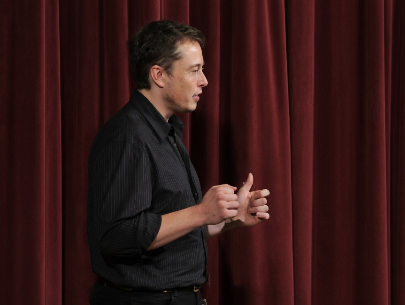 Elon Musk gesturing while speaking at Stanford – October 8, 2003 - Profile view of Elon Musk passionately explaining his ideas at his first documented public talk at Stanford University in 2003. Just 32 years old, he was already thinking in decades. Original screen grab enhanced for clarity using Grok Imagine.