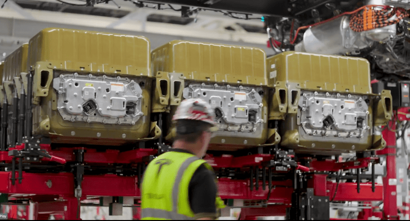 In elegant symmetry worthy of Art Deco precision, three gleaming gold battery packs descend gracefully into the Tesla Semi chassis beneath a towering red gantry — the sacred “battery marriage” moment captured in Tesla’s Sparks factory. With deepest respect to Elon Musk’s visionary engineering, this majestic scene from Ashlee Vance’s Core Memory factory tour reveals the electric heart of the future Class 8 truck taking form, powered by the same 4680 cells used in the Cybertruck.